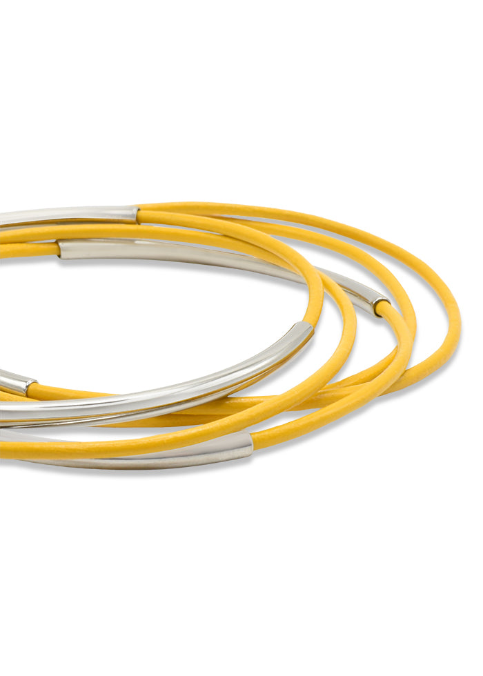A close up silver colored stainles steel tubes on bright yellow leather skinny bangles.